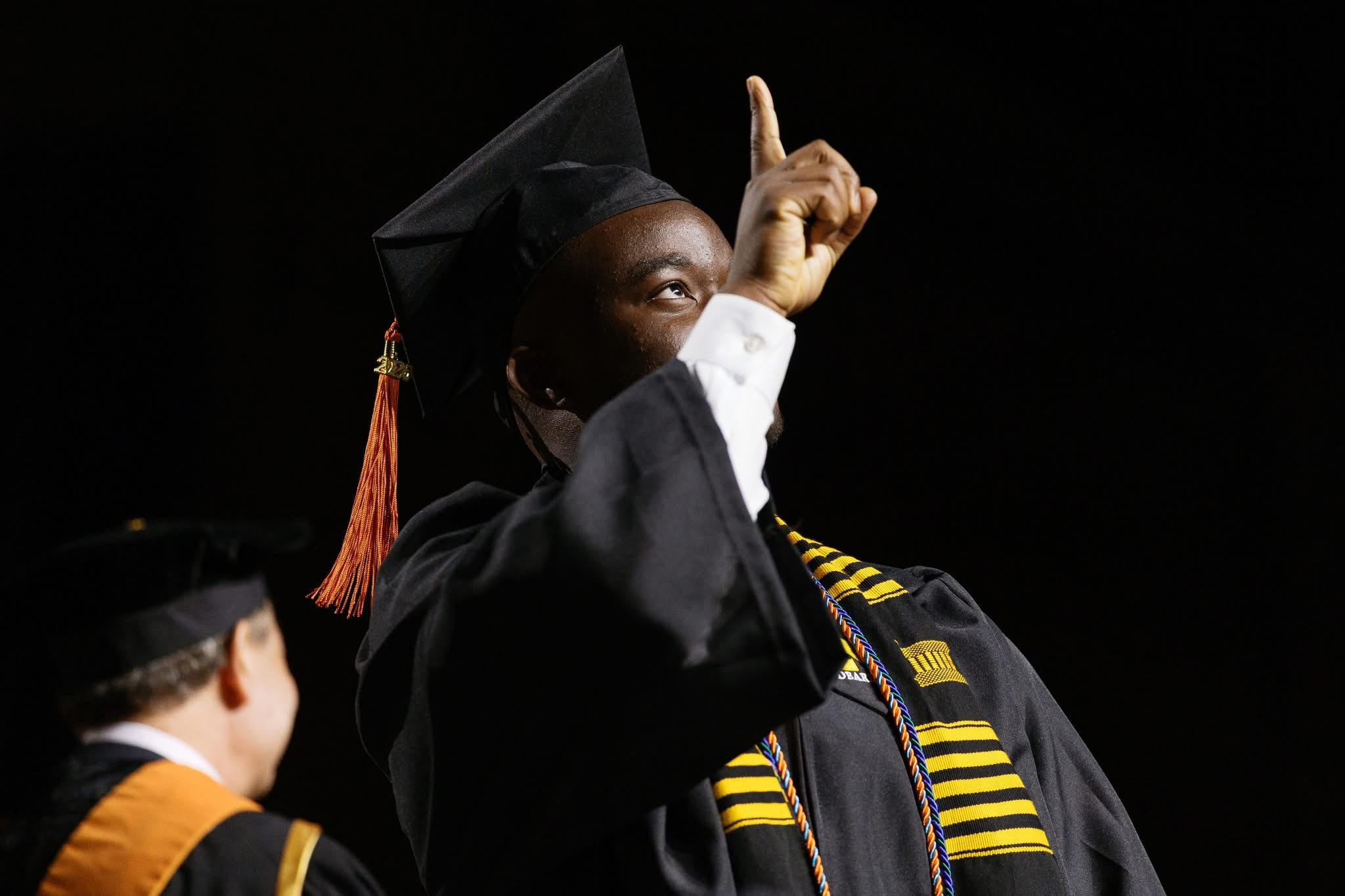 Jidechukwu Owo in cap and gown at commencement, pointing upward as he crosses the stage